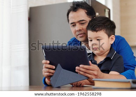Father hugging little kid when they are watching animated video om tablet computer
