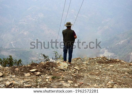 A man, wearing a hat standing on hilltop viewing the valley down