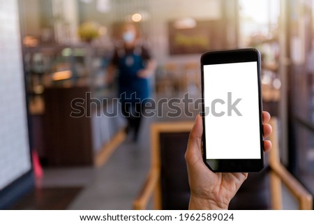 Hand man holding black mobile phone with blank white screen with blur coffee shop background. Mockup image of hand holding smartphone with blank white screen with copy space