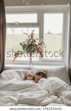 Picture of two siblings spending time together. Blonde cute boy lying in bed with his little sister.