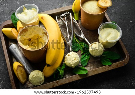 Banana yellow ice cream with mint and fresh banana. Ice cream spoon. On a black stone background, top view.
