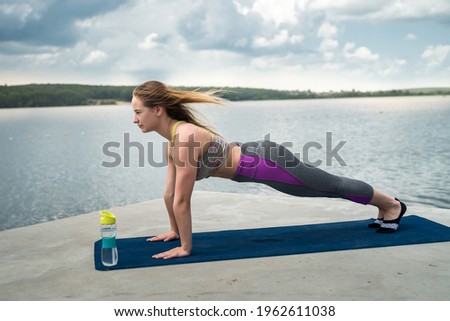 Relaxed girl in sportswear doing stretching, meditation exercise, breathing practice on yoga mat near lake
