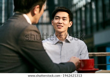 two asian corporate businesspeople discussing business at a outdoor coffee shop Royalty-Free Stock Photo #1962621313