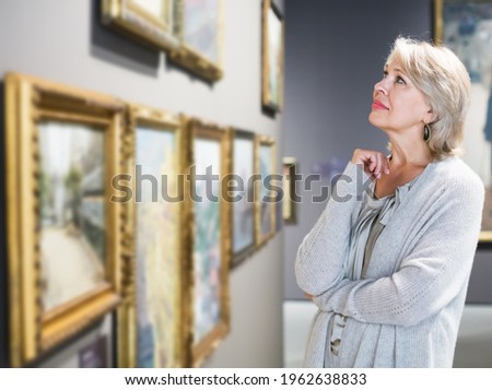 Portrait of positive adult female near picture collection in the museum