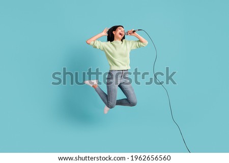 Full size photo of attractive lady jumping hold mic open mouth singing loud isolated on blue color background