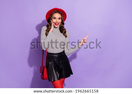 Photo of cute impressed woman wear striped outfit headwear clutch arm cheek pointing empty space isolated violet color background
