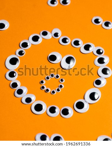 Surprised smiley face from toy eyes in the surroundings of other eyes on an orange background