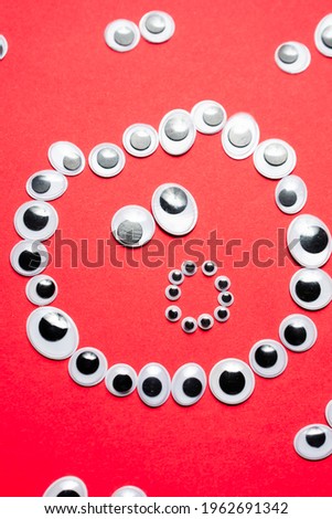 Surprised smiley face from toy eyes in the surroundings of other eyes on an red background