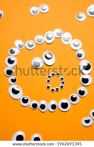 Surprised smiley face from toy eyes in the surroundings of other eyes on an orange background