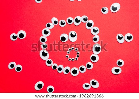 Surprised smiley face from toy eyes in the surroundings of other eyes on an red background