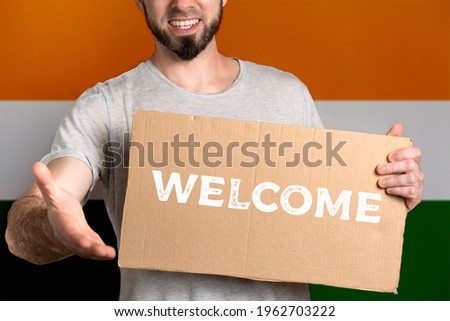 The concept of tolerance for immigrants and people of different life positions. A man holds a cardboard and stretches out his hand to greet. Flag of India. Text Welcome.