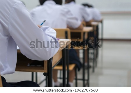 Writing test in exam with behind girl Asian students group concentrate in high school, serious taking final examination desk at classroom with Thai student uniform. Education evaluation back to school Royalty-Free Stock Photo #1962707560