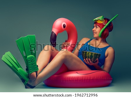 Girl sitting on big inflatable flamingo, ready to swim, blue studio background with empty space