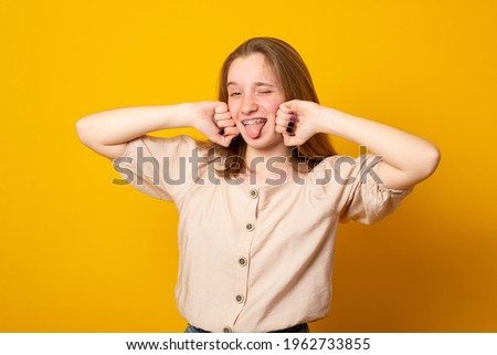 Cute little girl laughs and smiles on a yellow background. Happy teenage girl with braces on her teeth shows two fingers.