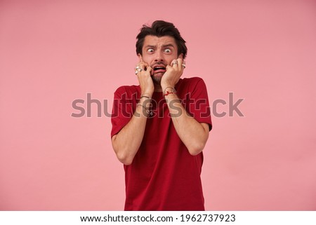 Hysrerical crazy young man with stubble in red tshirt feels terrified and looks panicked over pink background Royalty-Free Stock Photo #1962737923