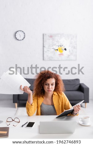 exhausted freelancer holding documents and notebook while sitting near laptop