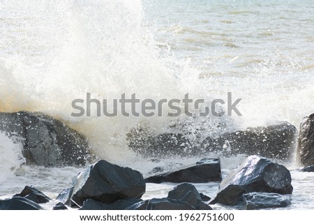 Sea waves in bright sunlight roll on the beach. Beautiful pastel gray sea background. The concept of summer, vacation, travel. The purest clear sea water, large stones closeup. The texture of sea foam