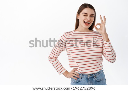 Alright, everything under control. Smiling confident girl assures all good, shows okay OK sign and winks, no problem, good job, praising or making compliment, standing over white background