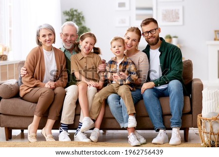 Big happy family. Portrait of grandparents, mother, father and two their cute kids, sister and brother, sitting together on coach at home and smiling at camera. Mortgage loan and real estate concept Royalty-Free Stock Photo #1962756439