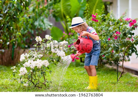 Child gardening. Little boy with red watering can in blooming sunny garden. Kids help in backyard. Summer outdoor fun. Kid taking care of plants and flowers. Royalty-Free Stock Photo #1962763804