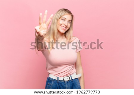 young blond pretty woman smiling and looking friendly, showing number three or third with hand forward, counting down