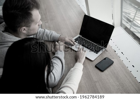 Man and woman work on laptop together. Colleagues sit in coffee shop to work on common project. Coworking concept. Coffeehouse on background. Modern gray laptop
