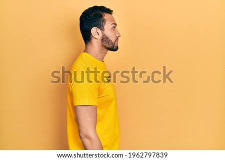 Hispanic man with beard wearing t shirt with happiness word message looking to side, relax profile pose with natural face and confident smile. 