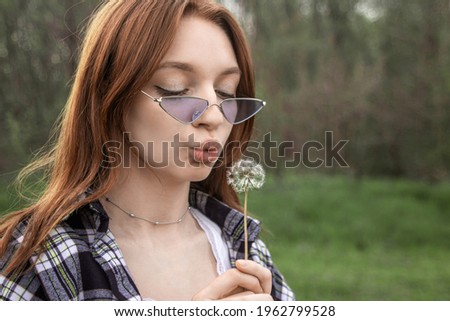 Girl blowing on a dandelion on the background of nature. Portrait of a girl with red hair