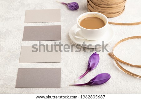 Gray paper business card mockup with spring snowdrop crocus flowers and cup of coffee on gray concrete background. Blank, business card, side view, copy space, still life. spring concept.