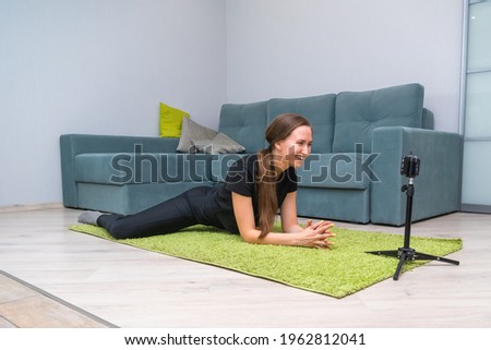 Young beautiful, dark-haired female blogger writes content for her video blog. An attractive woman is engaged in stretching at home on a light green mat. Concept of a healthy lifestyle