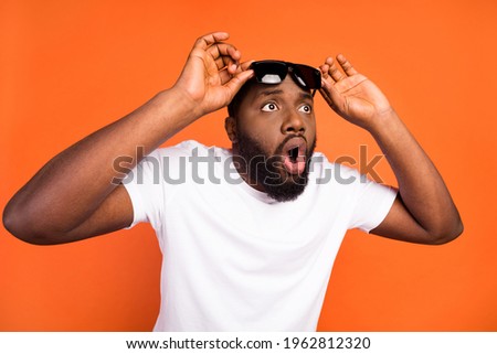 Photo of amazed astonished afro american young man look empty space hold glasses isolated on orange color background Royalty-Free Stock Photo #1962812320