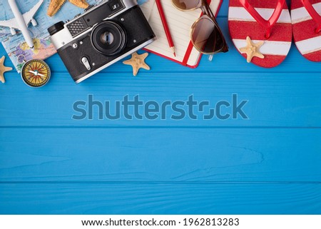 Overhead photo of camera starfish planner pencil sunglasses map airplane compass and sandals isolated on the blue wooden background with empty space