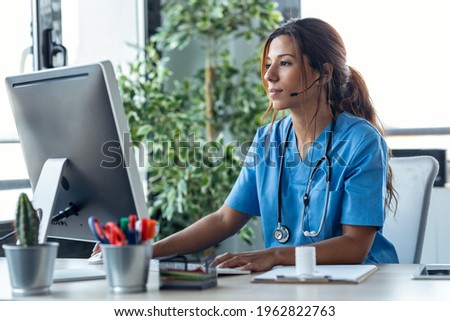 Shot of female doctor talking with earphone while explaining medical treatment to patient through a video call with computer in the consultation. Royalty-Free Stock Photo #1962822763