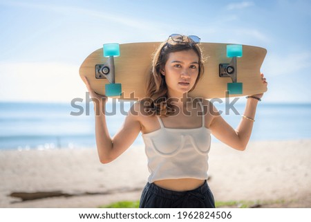 Asian women surf skate or skates board outdoors on beautiful summer day. Happy young women play surf skate at park on morning time.