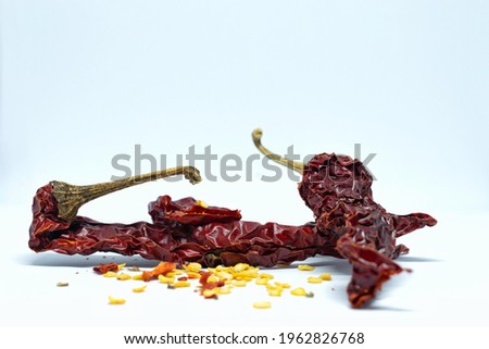 A picture of dried red chillies and their seeds as chilly flakes all around with white background.