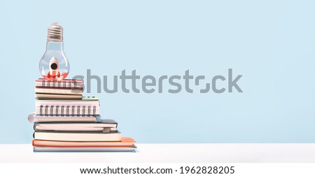 Idea. Business or education growth development and success concept banner. Rocket in lightbulb on pile of notebooks on office or home desk with blue background. Innovative thinking startup. Copy space