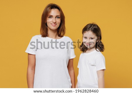 Happy woman in white t-shirt have fun with cute child baby girl 5-6 years old look camera. Mommy little kid daughter isolated on yellow orange color background studio. Mother's Day love family concept