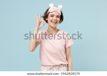 Calm young fun happy satisfied caucasian woman in pajamas jam sleep eye mask rest relax at home show ok okay gesture isolated on pastel blue background studio portrait. Good mood night bedtime concept