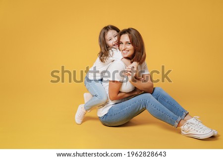 Full body length happy woman in basic white t-shirt have fun sit on floor child baby girl 5-6 years old Mom mum little kid daughter isolated on yellow color background studio Mother's Day love family Royalty-Free Stock Photo #1962828643