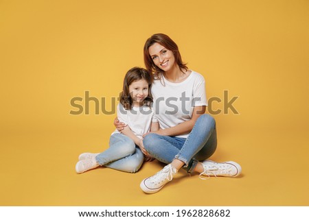 Full body length happy woman in basic white t-shirt have fun sit on floor with child baby girl 5-6 years old Mom little kid daughter isolated on yellow color background studio Mother's Day love family