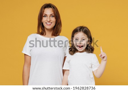 Happy woman in basic white t-shirt have fun with child baby girl 5-6 years old raised finger up idea Mom little kid daughter isolated on yellow color background studio Mother's Day love family concept