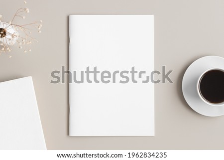 Magazine mockup with a cup of coffee, book and a gypsophila on the beige table. Royalty-Free Stock Photo #1962834235