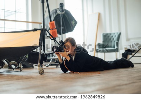 Female photographer lies on the ground in a photo studio and takes pictures on the camera from the bottom of the shooting point.