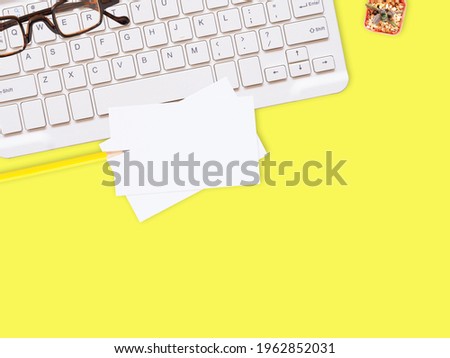 Flat lay white business card over keyboard with glasses, pencil, and cactus on yellow office desktop with copy space for text. Top view.  Business and education concept.
