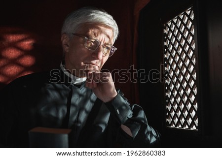 Senior priest sitting behind the grid and listening the confession in the church Royalty-Free Stock Photo #1962860383