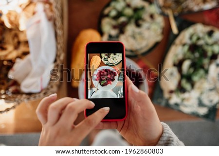 Female hands hold a phone and take pictures of food on the table