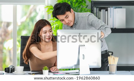 Male professional photographer working happily together with female graphic designer discussing creatively about a project while looking at the computer screen on the desk in the office.