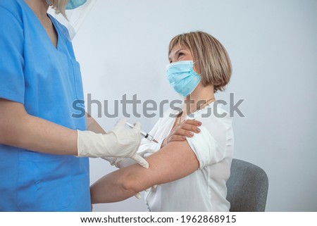 Female patient with protective face mask waiting for vaccination, doctor in surgical gloves disinfecting her arm. Doctor applying a vaccine on a woman's arm. Medical concept 