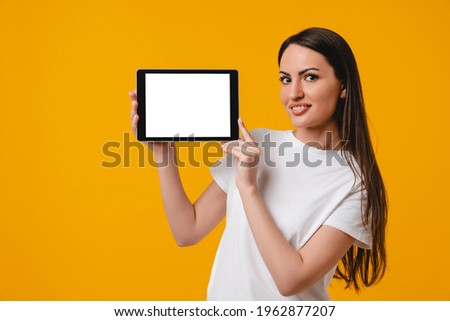 Young attractive caucasian woman showing tablet`s screen isolated over yellow background. Smart intelligent female student using digital tablet for online working, social media, webinars, video calls