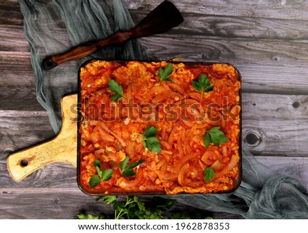 Dough baked herring fish with tomato sauce and onion in a glass bowl. Fish, baked with vegetables in tomato sauce. Dark wooden background. Top view. 